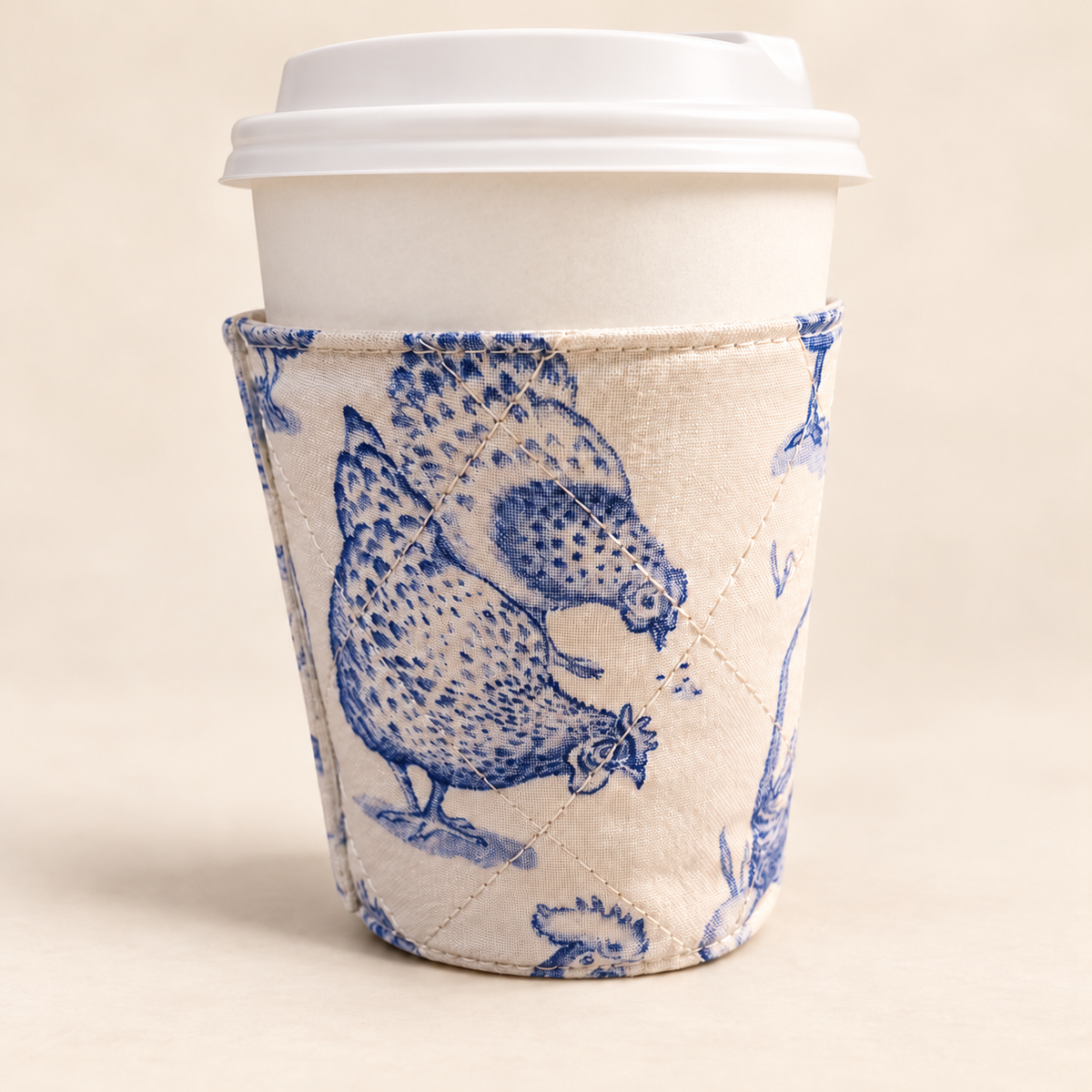 Blue chicken print quilted coffee cup cozy on a white to-go coffee cup